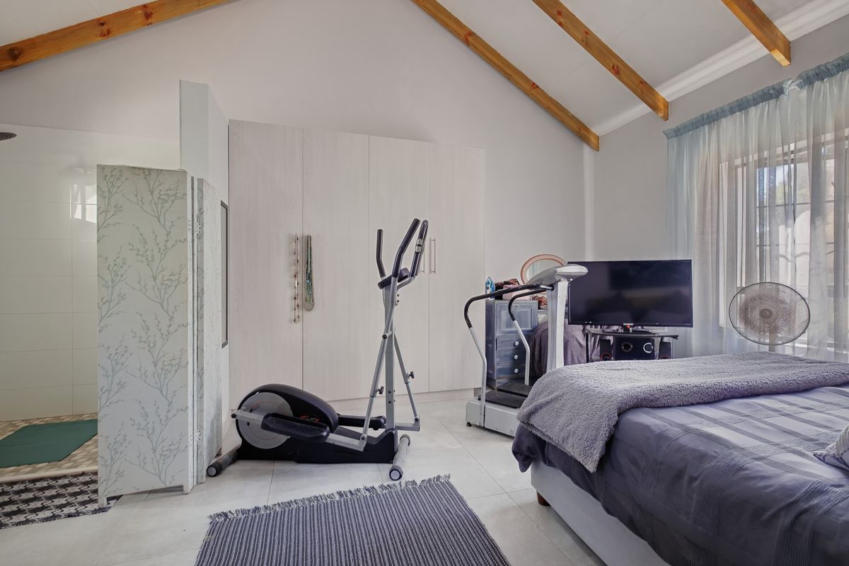 Spacious bedroom featuring a vaulted ceiling with exposed timber beams, built-in cupboards, tiled flooring, and an integrated en-suite shower area.