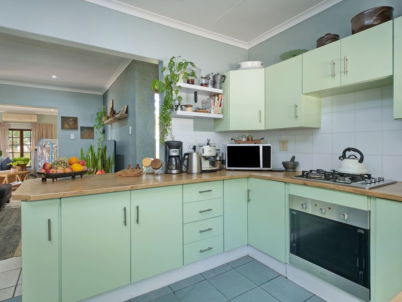 Open-plan kitchen featuring light green cabinetry, wood-look countertops, gas hob, and built-in oven, seamlessly flowing into the adjacent living area.