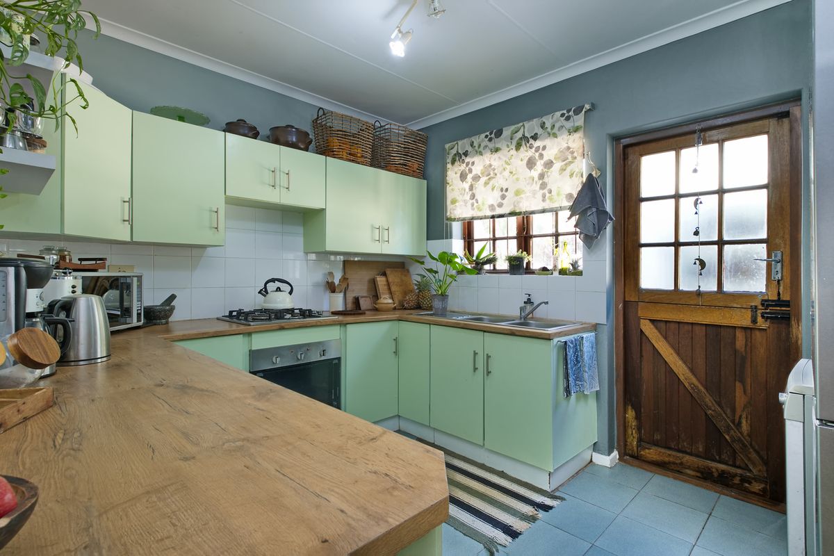 A functional kitchen featuring light green cabinetry, wood-look laminate countertops, a gas hob, built-in oven, and a classic timber stable door leading outside.