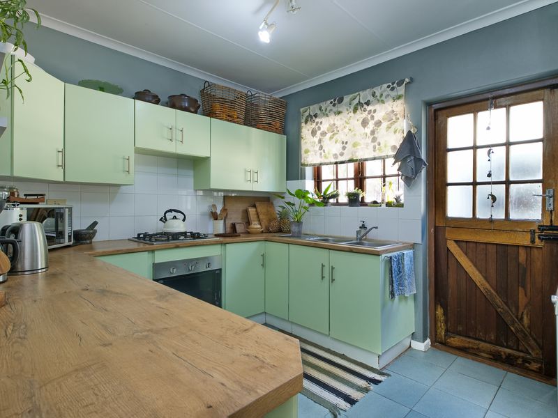 A functional kitchen featuring light green cabinetry, wood-look laminate countertops, a gas hob, built-in oven, and a classic timber stable door leading outside.
