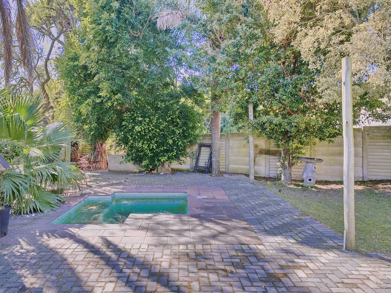 Outdoor pool area featuring a small swimming pool, paved patio space, and perimeter walling surrounded by mature trees and garden greenery.