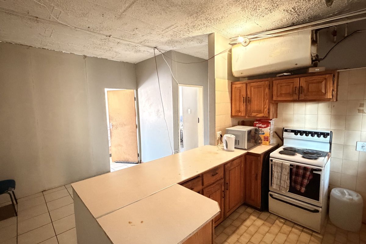 A dated kitchen featuring wooden cabinetry, a freestanding stove, and tiled splashbacks, requiring significant renovation and modernization to improve functionality and aesthetic appeal.