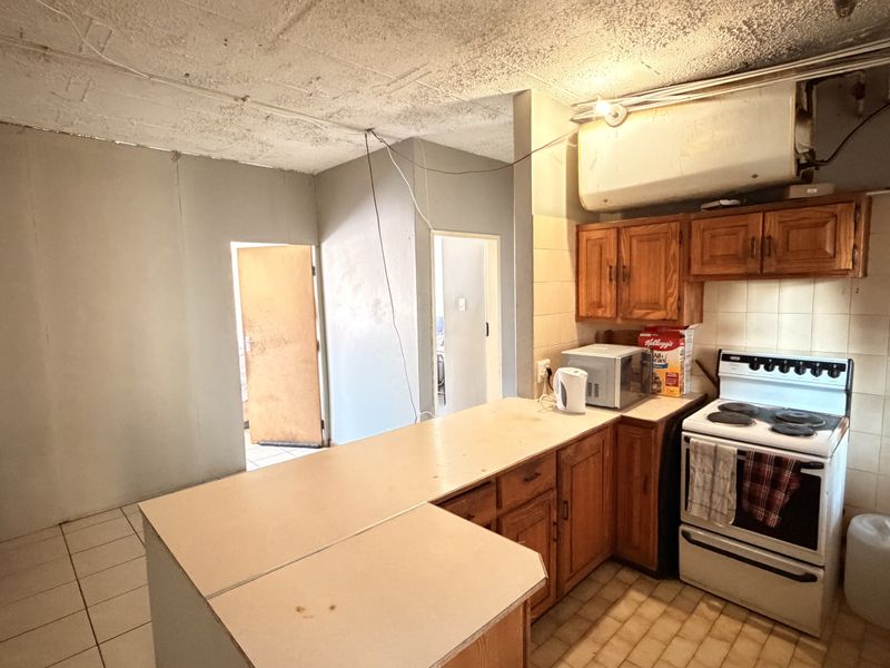A dated kitchen featuring wooden cabinetry, a freestanding stove, and tiled splashbacks, requiring significant renovation and modernization to improve functionality and aesthetic appeal.