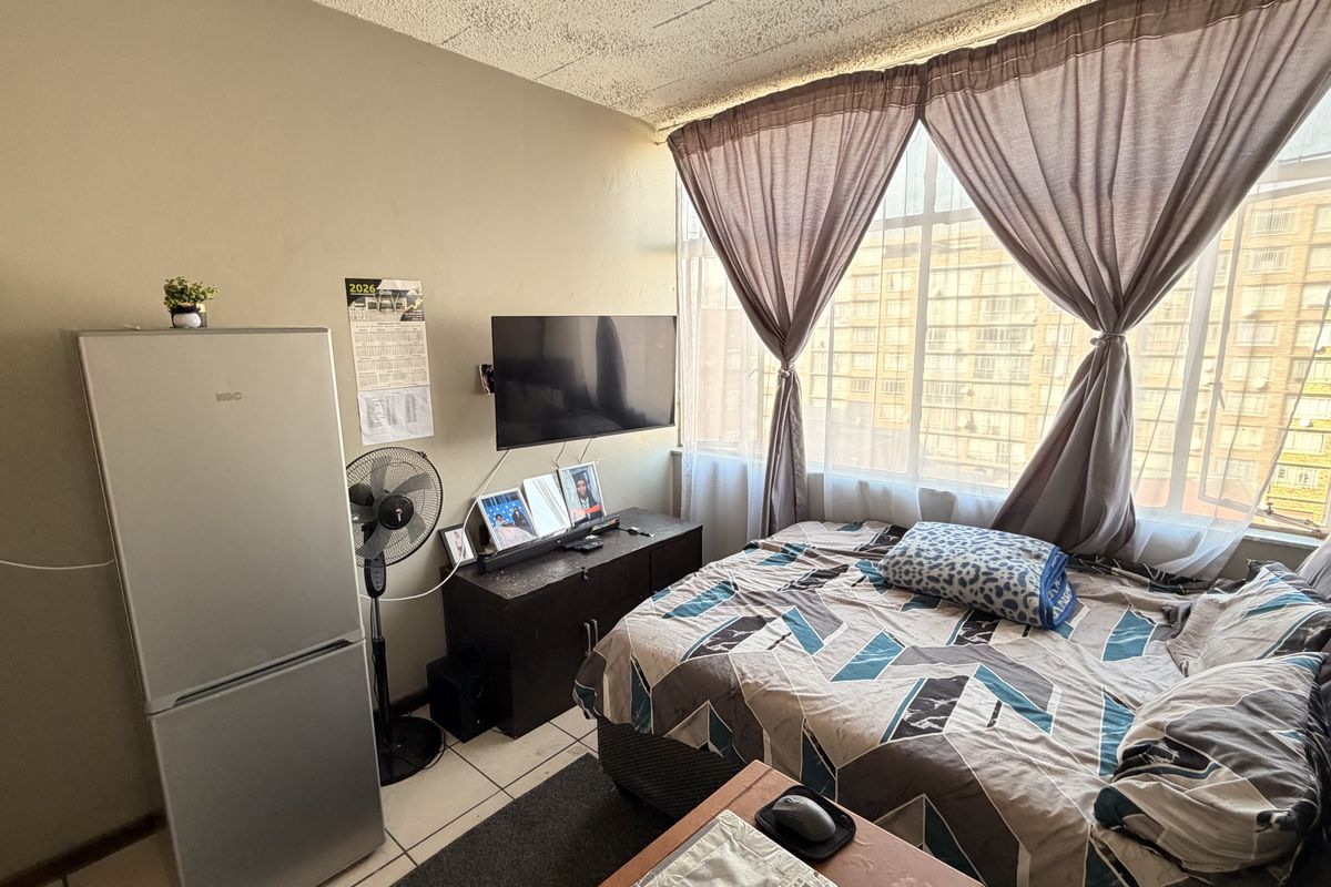 A compact bedroom featuring tiled flooring, a large window with natural light, and a textured ceiling finish.