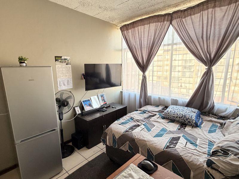 A compact bedroom featuring tiled flooring, a large window with natural light, and a textured ceiling finish.