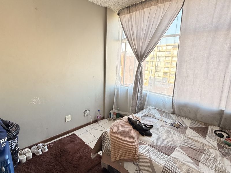 A bedroom featuring tiled flooring and a large window with curtains, requiring cosmetic updates to the wall finishes.