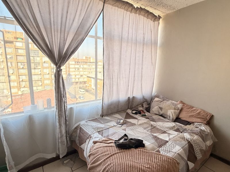 A bedroom featuring large windows with natural light and tiled flooring, requiring minor cosmetic updates to the walls and ceiling.
