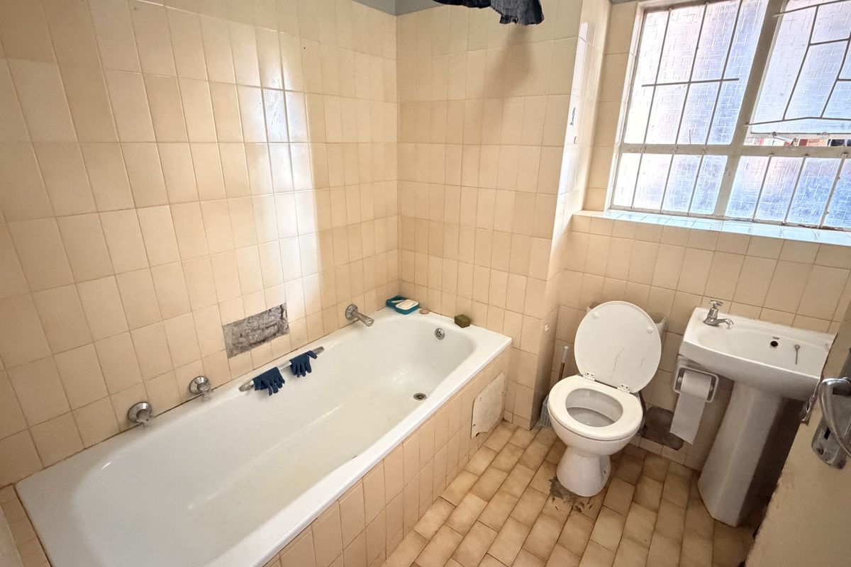 A dated bathroom featuring a standard bathtub, pedestal basin, and toilet, with tiled walls and flooring, requiring cosmetic updates.