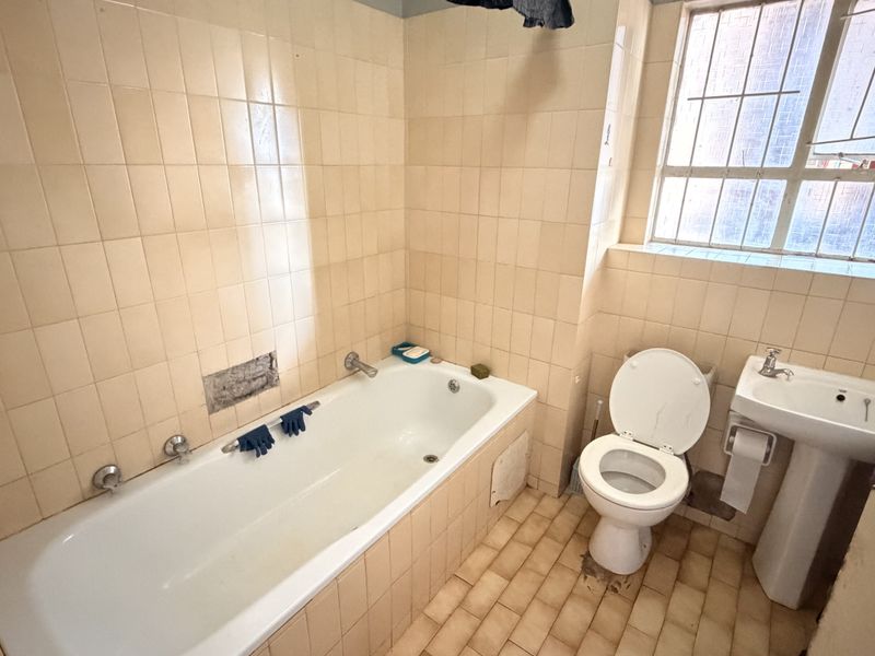 A dated bathroom featuring a standard bathtub, pedestal basin, and toilet, with tiled walls and flooring, requiring cosmetic updates.