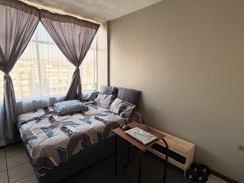 A bedroom featuring a large window with natural light, tiled flooring, and textured ceiling, requiring minor wall and ceiling repairs.