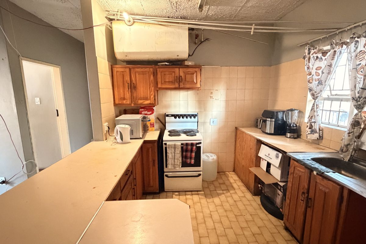 A dated kitchen featuring wooden cabinetry, a freestanding stove, stainless steel sink, and tiled splashbacks, offering significant potential for modernization and renovation.