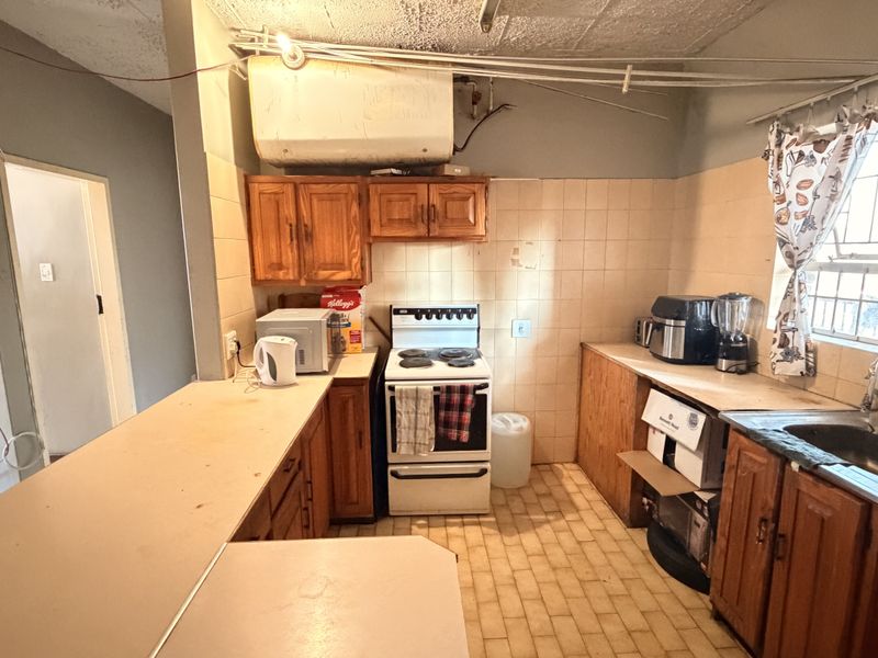 A dated kitchen featuring wooden cabinetry, a freestanding stove, stainless steel sink, and tiled splashbacks, offering significant potential for modernization and renovation.