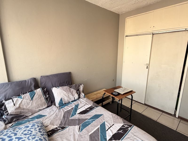 A bedroom featuring built-in wardrobes and tiled flooring, currently requiring cosmetic updates to the walls and cabinetry to improve its overall condition.