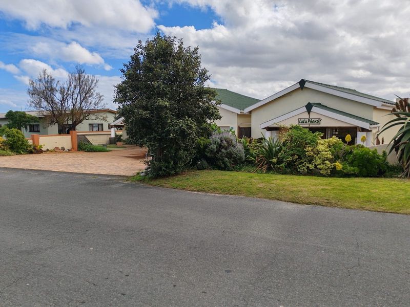 Front view of the property featuring a paved driveway, established garden, and a pitched roof structure.