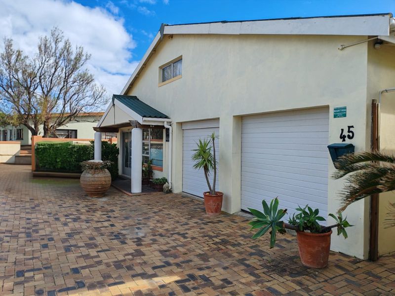 Front elevation of the property featuring a double garage with sectional doors, a paved driveway, and a covered entrance porch with structural columns.