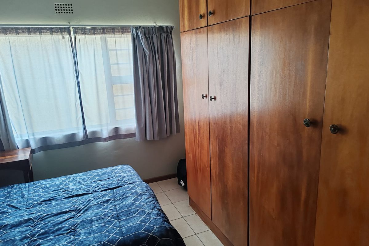 A bedroom featuring built-in wooden cupboards, tiled flooring, and a window with natural light.