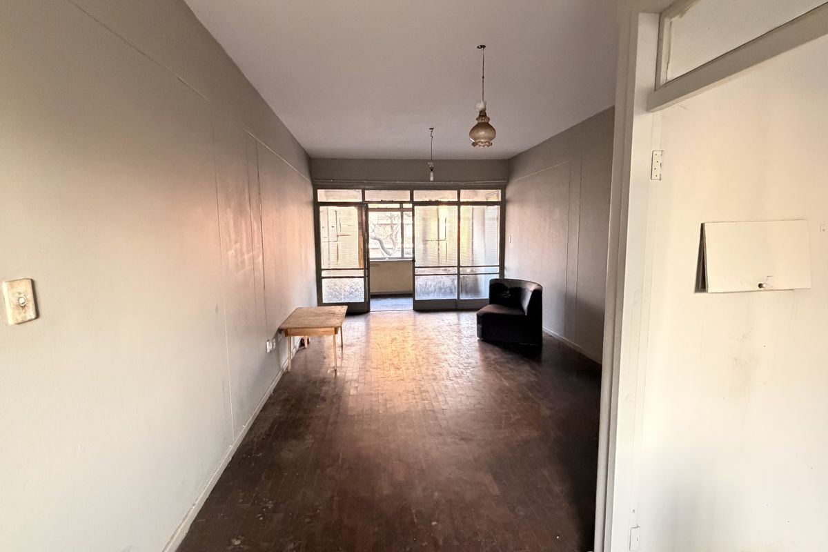 Spacious living area featuring original parquet flooring and large glass sliding doors leading to an outdoor space, offering a blank canvas for renovation.