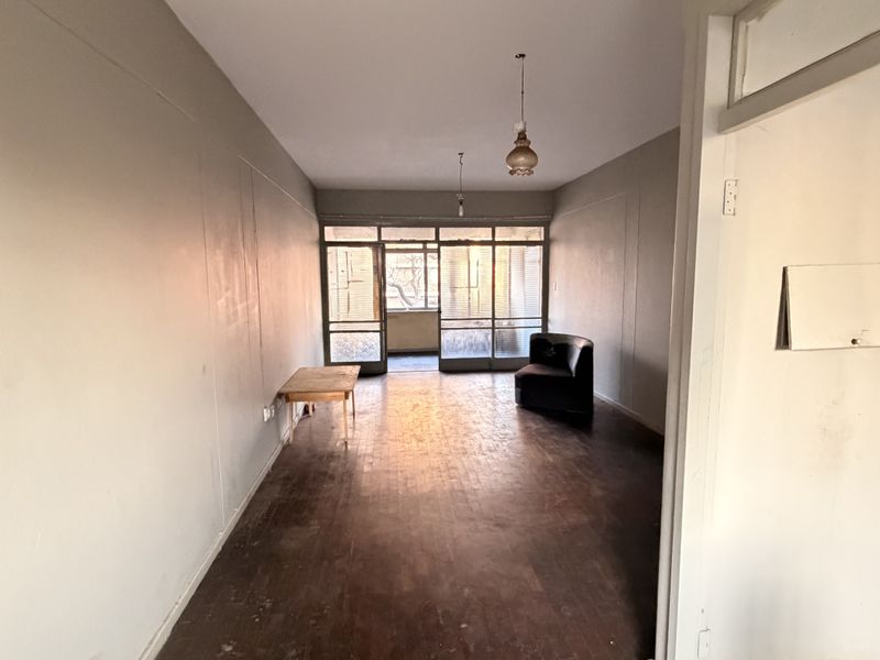 Spacious living area featuring original parquet flooring and large glass sliding doors leading to an outdoor space, offering a blank canvas for renovation.
