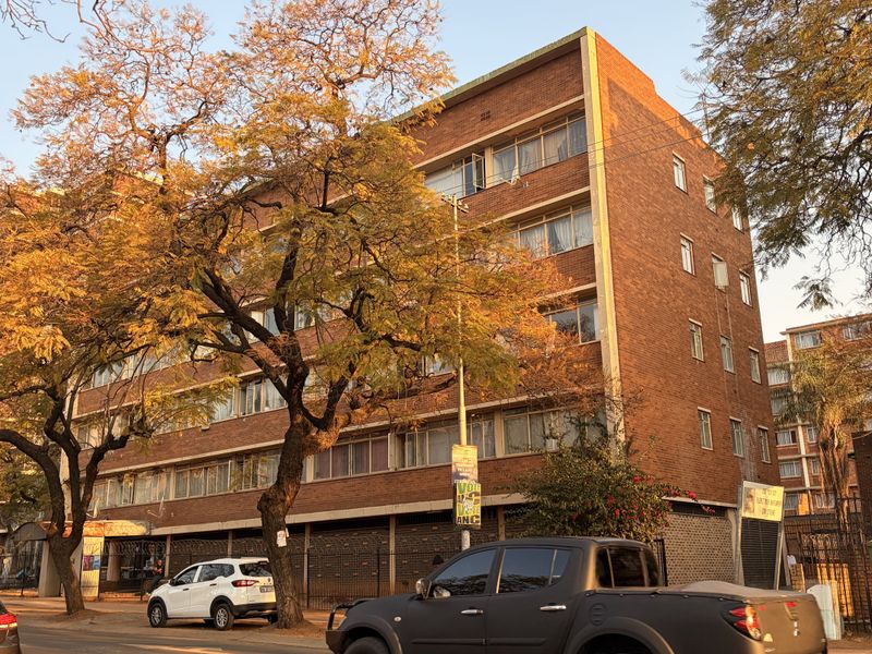A multi-story brick apartment building viewed from the street, featuring classic architectural design and established trees in the foreground.