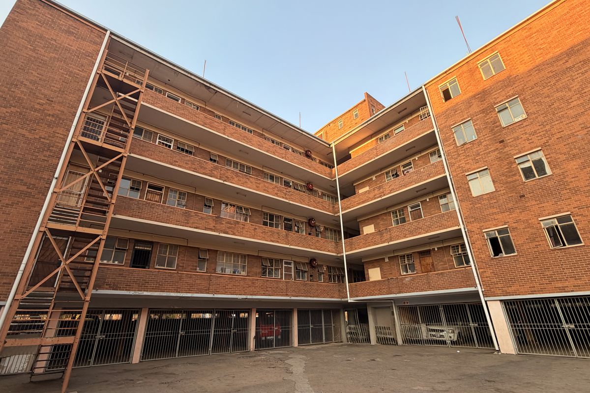 Exterior view of a multi-story brick apartment building featuring an external metal staircase and ground-level secure parking bays.