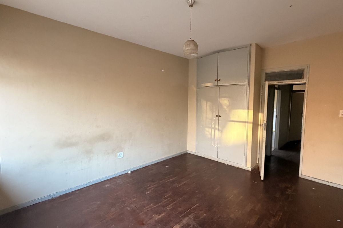 An empty bedroom featuring original parquet flooring, built-in storage cupboards, and neutral wall finishes in need of cosmetic attention.