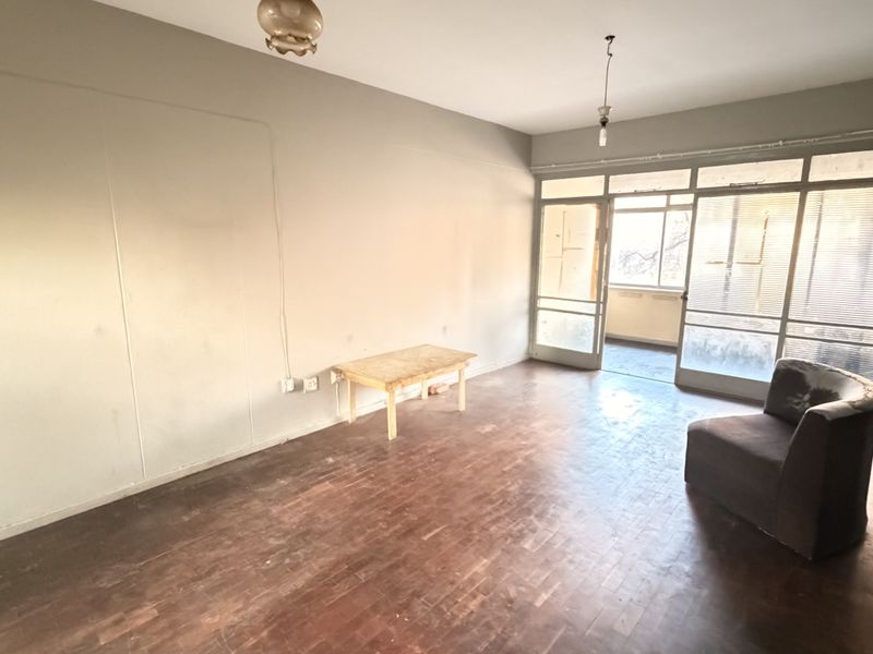 Spacious living area featuring original parquet flooring and large glass sliding doors leading to an outdoor balcony, offering a blank canvas for renovation.