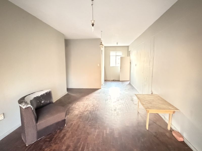 An empty living room featuring original parquet flooring and neutral wall tones, offering a blank canvas for renovation and interior design.