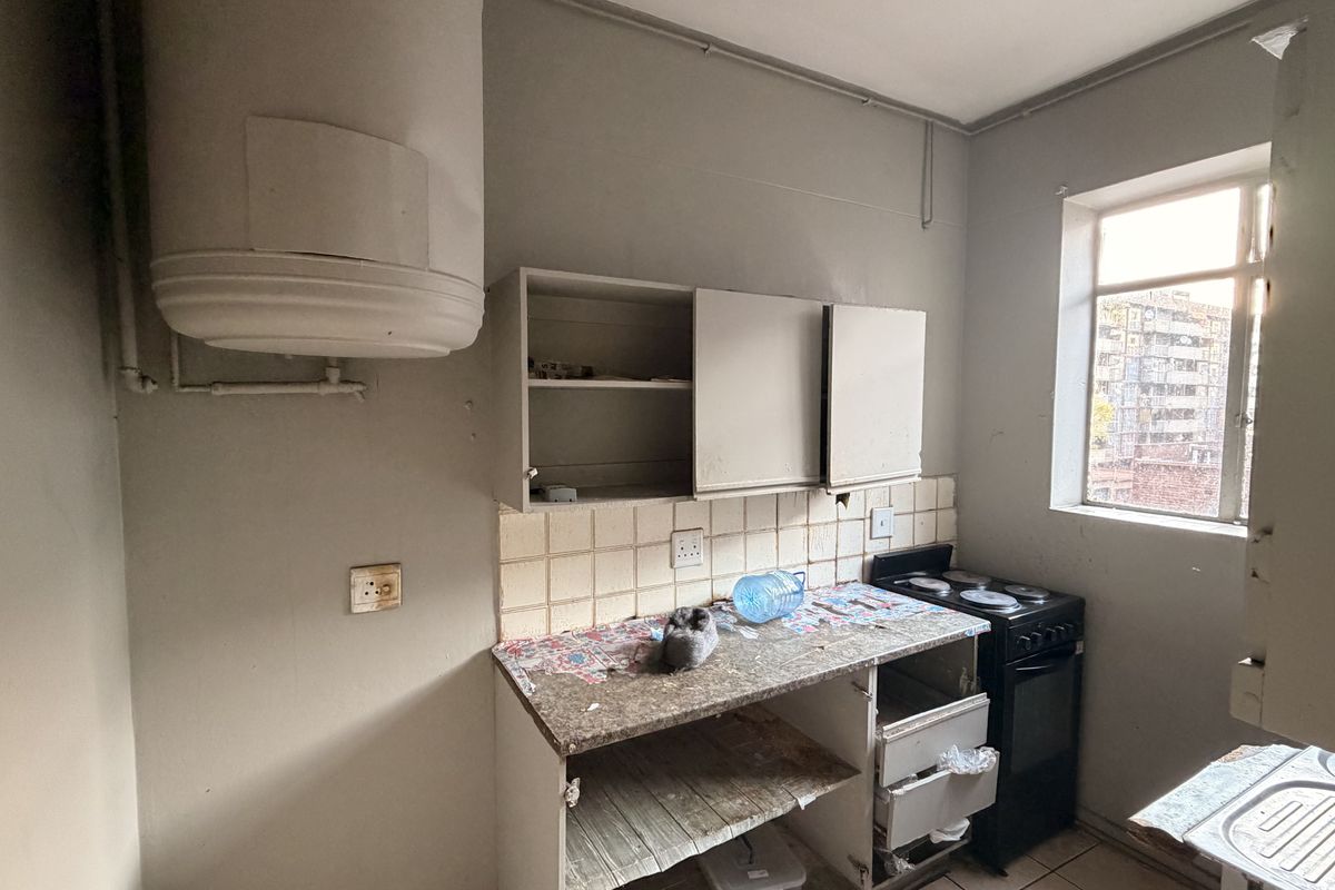 A compact kitchen featuring a wall-mounted geyser, electric stove, and basic cabinetry. The space requires significant renovation and cosmetic updates to improve functionality.