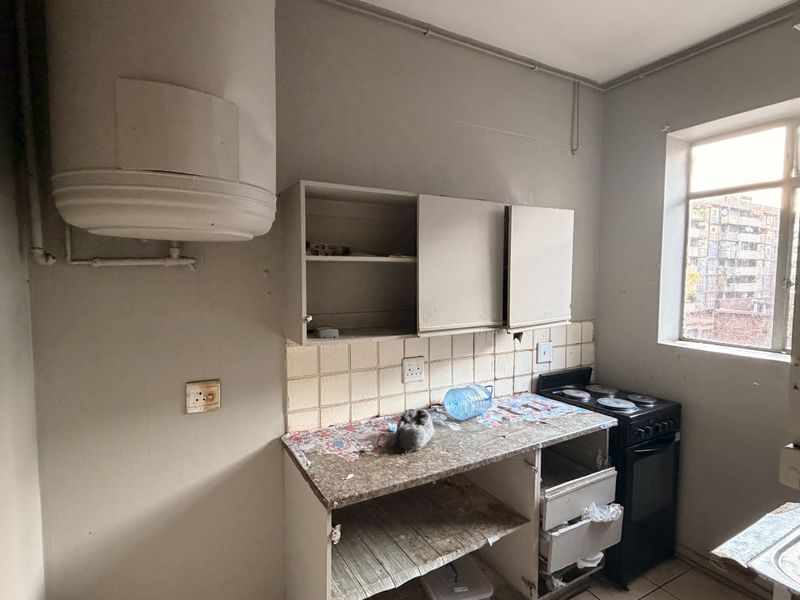 A compact kitchen featuring a wall-mounted geyser, electric stove, and basic cabinetry. The space requires significant renovation and cosmetic updates to improve functionality.