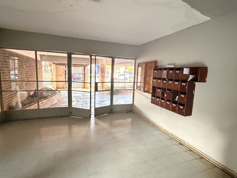 Entrance foyer featuring tiled flooring, metal-framed glass doors, and wall-mounted mailboxes, requiring cosmetic updates to improve the overall condition.