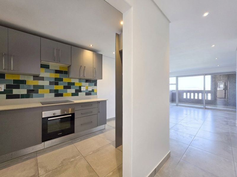 Modern open-plan kitchen featuring grey cabinetry and a vibrant tiled backsplash, flowing into a bright living area with access to a private balcony.