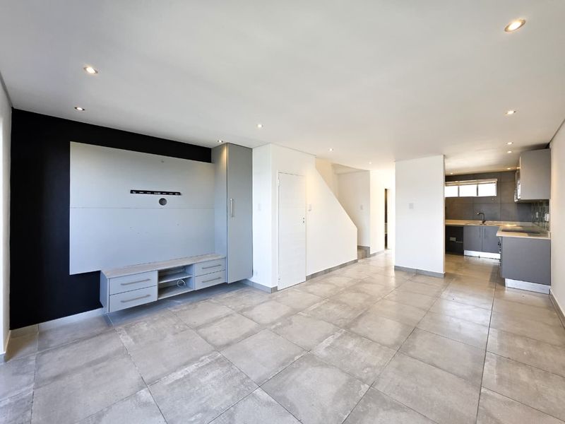 Spacious open-plan living area featuring modern grey cabinetry, tiled flooring, recessed lighting, and an integrated kitchen space with a neutral contemporary finish.