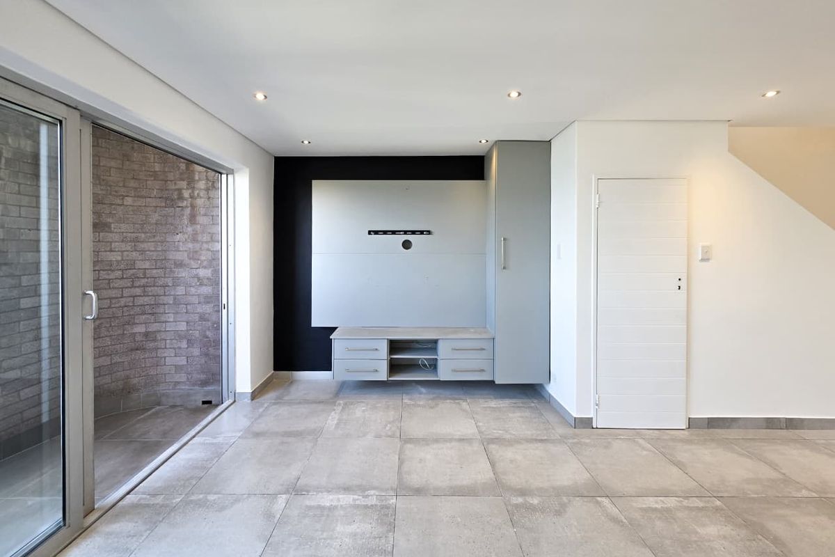 A bright, modern living area featuring large format floor tiles, a built-in media console, and a sliding glass door leading to an outdoor space.