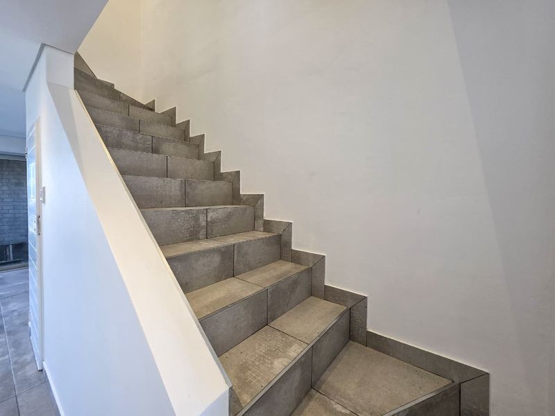 A clean, modern staircase featuring grey tiled steps and a white balustrade, providing a minimalist transition between levels.