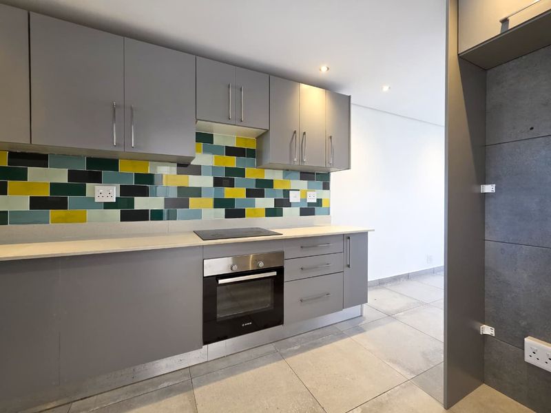 Modern kitchen featuring grey cabinetry, stone countertops, a colorful tiled splashback, and integrated electric oven and hob.