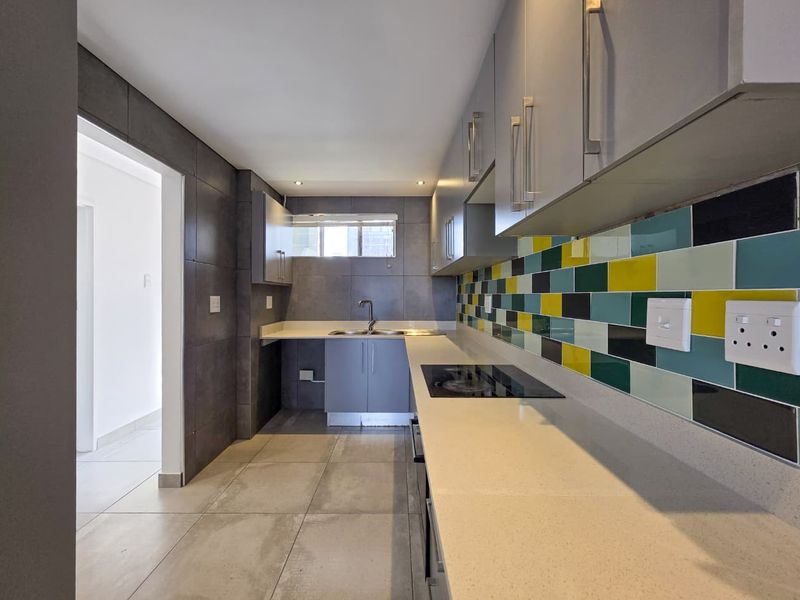 Modern kitchen featuring sleek grey cabinetry, stone countertops, a colorful tiled backsplash, and a built-in electric hob.