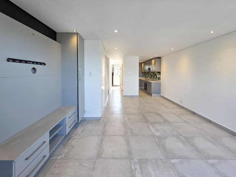Spacious open-plan living area featuring large format floor tiles, recessed lighting, and a modern kitchen with built-in cabinetry and appliances.