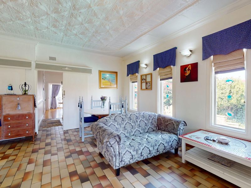 A living area featuring a decorative pressed metal ceiling, tiled flooring, and windows with stained glass accents, offering a classic character aesthetic.