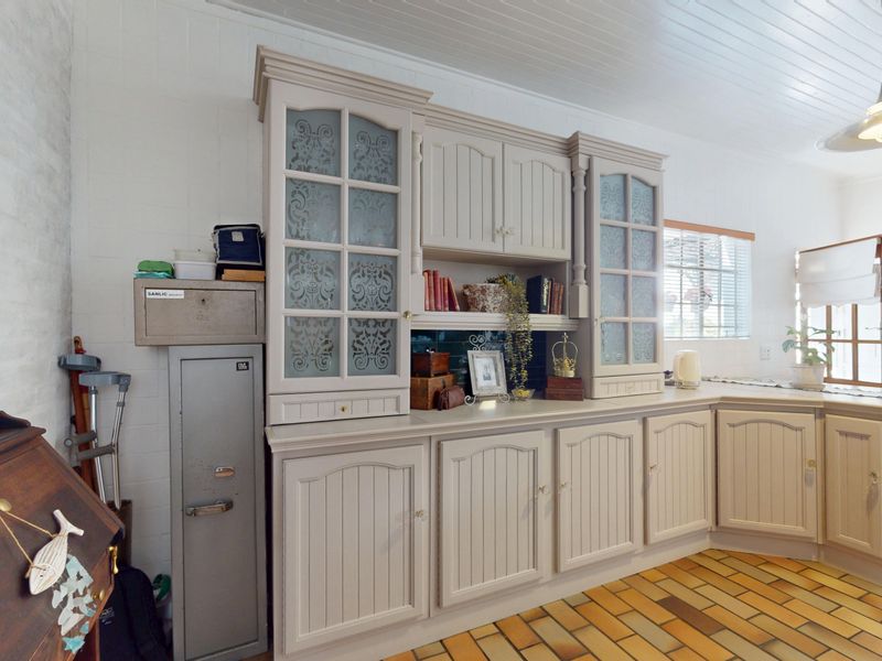A kitchen area featuring classic built-in cabinetry with glass-fronted display units, a tongue and groove ceiling, and traditional brick flooring.