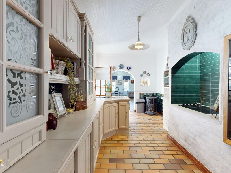 A charming kitchen featuring custom built-in cabinetry, terracotta-style tiled flooring, and a unique recessed stove alcove with green tiling.
