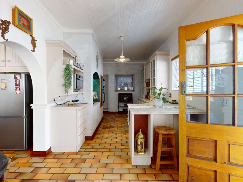 A rustic-style kitchen featuring terracotta tile flooring, beadboard ceiling, and built-in cabinetry with an arched entryway leading to the main kitchen area.