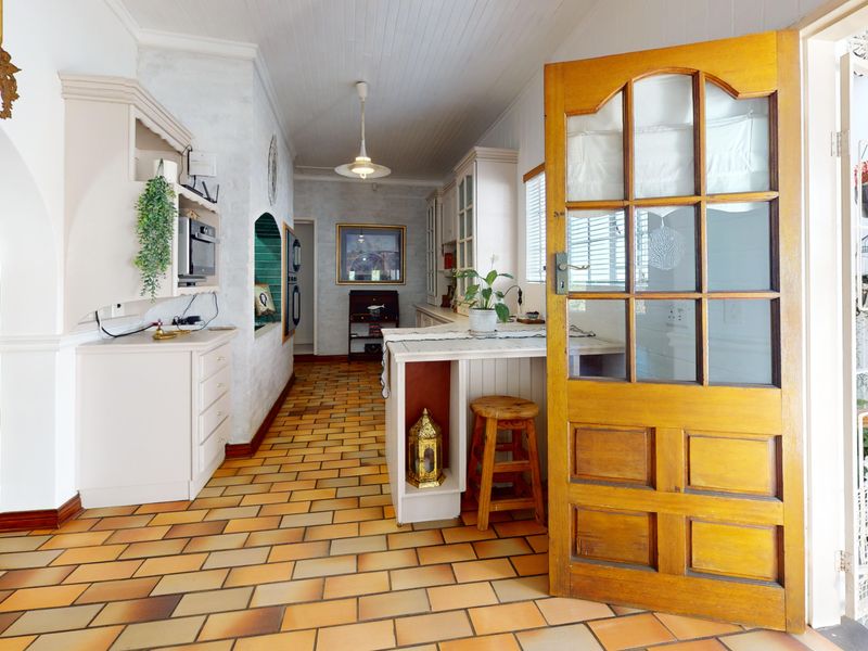 A rustic kitchen featuring terracotta-style tiled flooring, built-in cabinetry, and a classic timber door leading to an outdoor area.