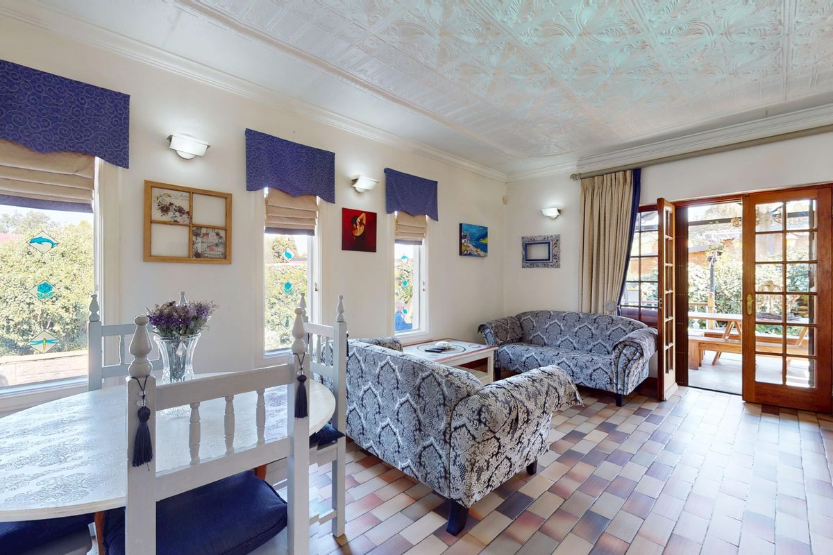 A living room featuring tiled flooring, a decorative pressed metal ceiling, and direct access to an outdoor patio area through timber-framed glass doors.