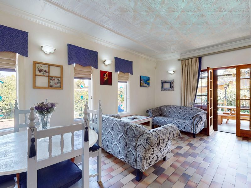 A living room featuring tiled flooring, a decorative pressed metal ceiling, and direct access to an outdoor patio area through timber-framed glass doors.