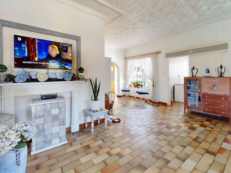 Spacious living area featuring a classic fireplace mantel, distinctive tiled flooring, and an ornate pressed metal ceiling, offering a bright and character-filled living space.