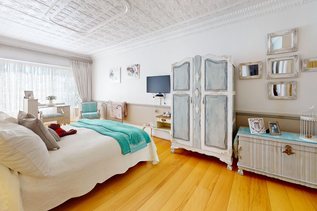 Spacious bedroom featuring beautiful pressed metal ceilings, polished hardwood flooring, and a classic dado rail, offering a bright and character-filled living space.
