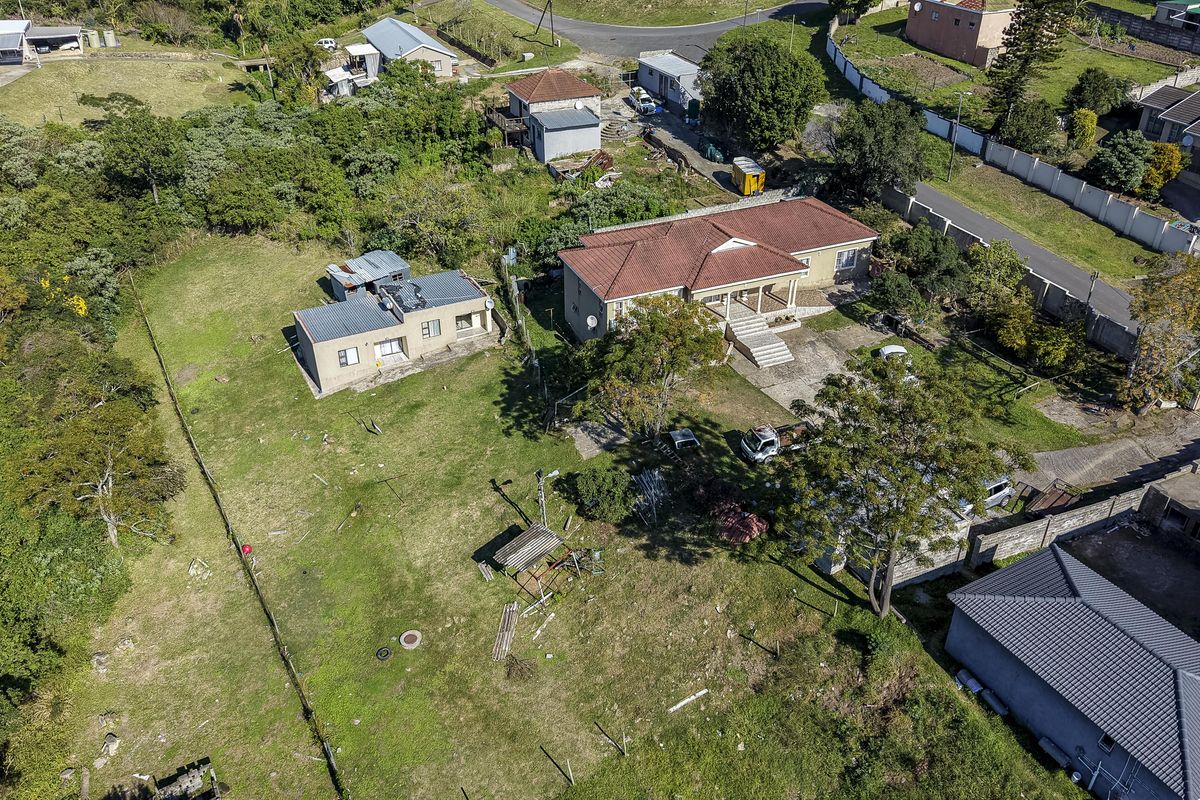 Aerial view of a residential property featuring a main house, an outbuilding, and a large surrounding garden area with established trees and boundary fencing.