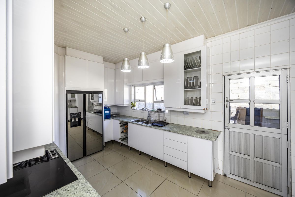 A functional kitchen featuring white cabinetry, stone-look countertops, double basin sink, and tiled finishes with integrated hob and pendant lighting.