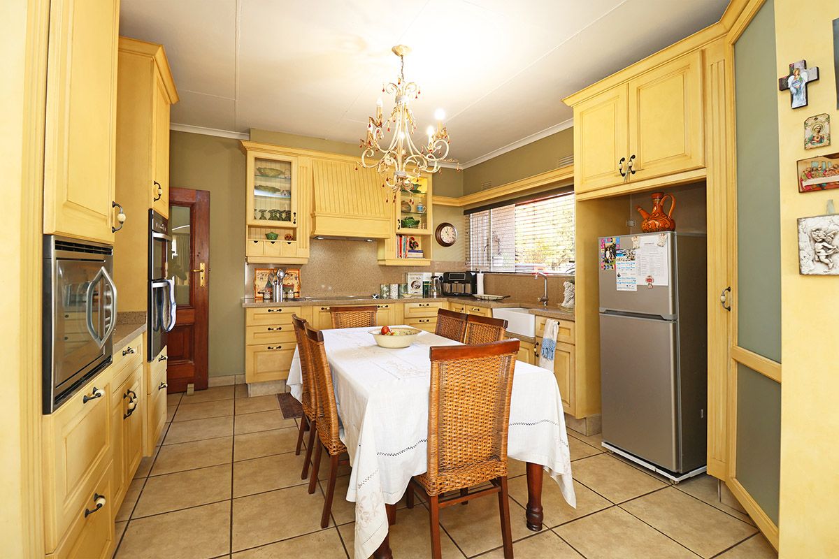 A traditional kitchen featuring yellow cabinetry, tiled flooring, a farmhouse sink, and a central dining area with a decorative chandelier.