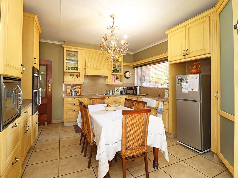 A traditional kitchen featuring yellow cabinetry, tiled flooring, a farmhouse sink, and a central dining area with a decorative chandelier.